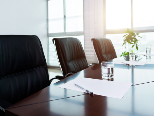 Empty black chairs in a bright conference room with big windows.