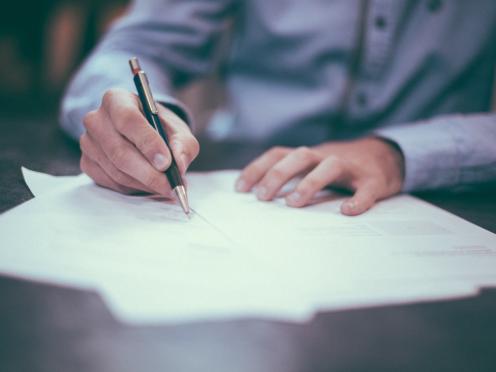 zoom sur les mains d'une personne signant des documents.