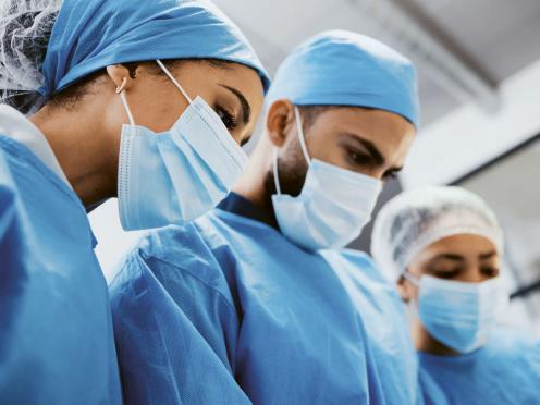 Trois médecins portant des blouses bleues et des masques.