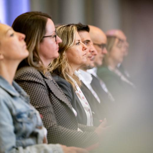 Personen im Publikum verfolgen eine Präsentation.