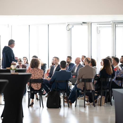 Sitzende Personen hören einer Person zu, die einen Workshop leitet.