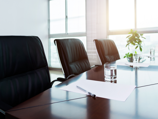 Empty black chairs in a bright conference room with big windows.
