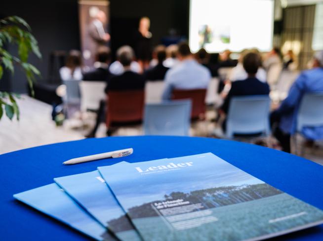 Leader Mag in primo piano, persone al workshop sullo sfondo.