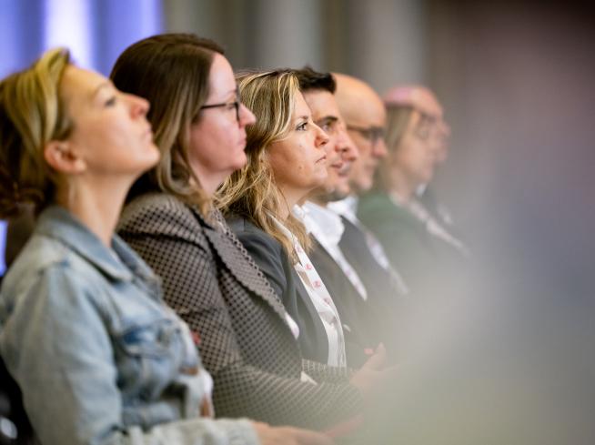 Persone tra il pubblico assistono a una presentazione.