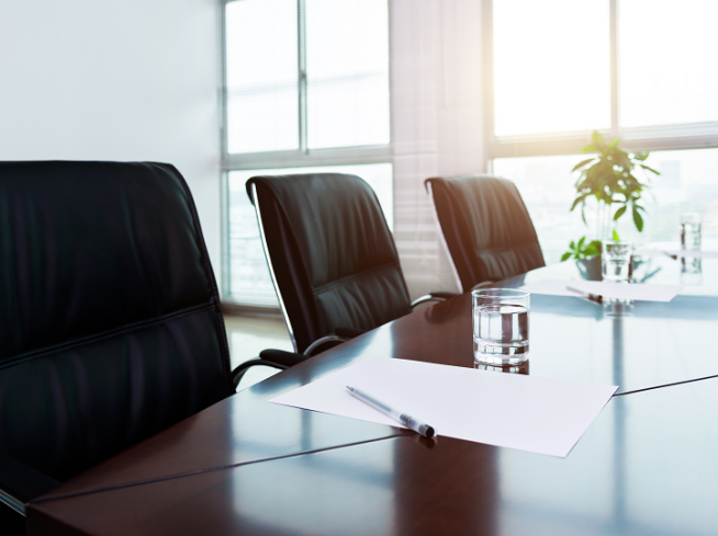 Empty black chairs in a bright conference room with big windows.