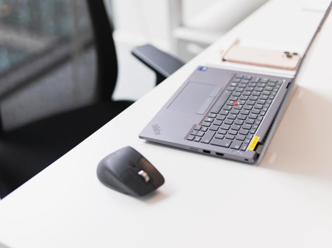 Laptop aperto su una scrivania, con un mouse e un telefono accanto.